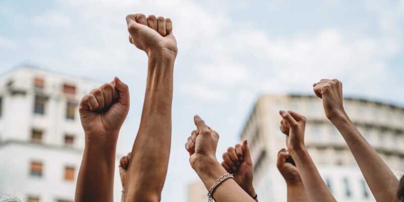 People with raised fists at a demonstration in the city People with raised fists at a demonstration in the city. Multi-ethnic group of people together on strike.