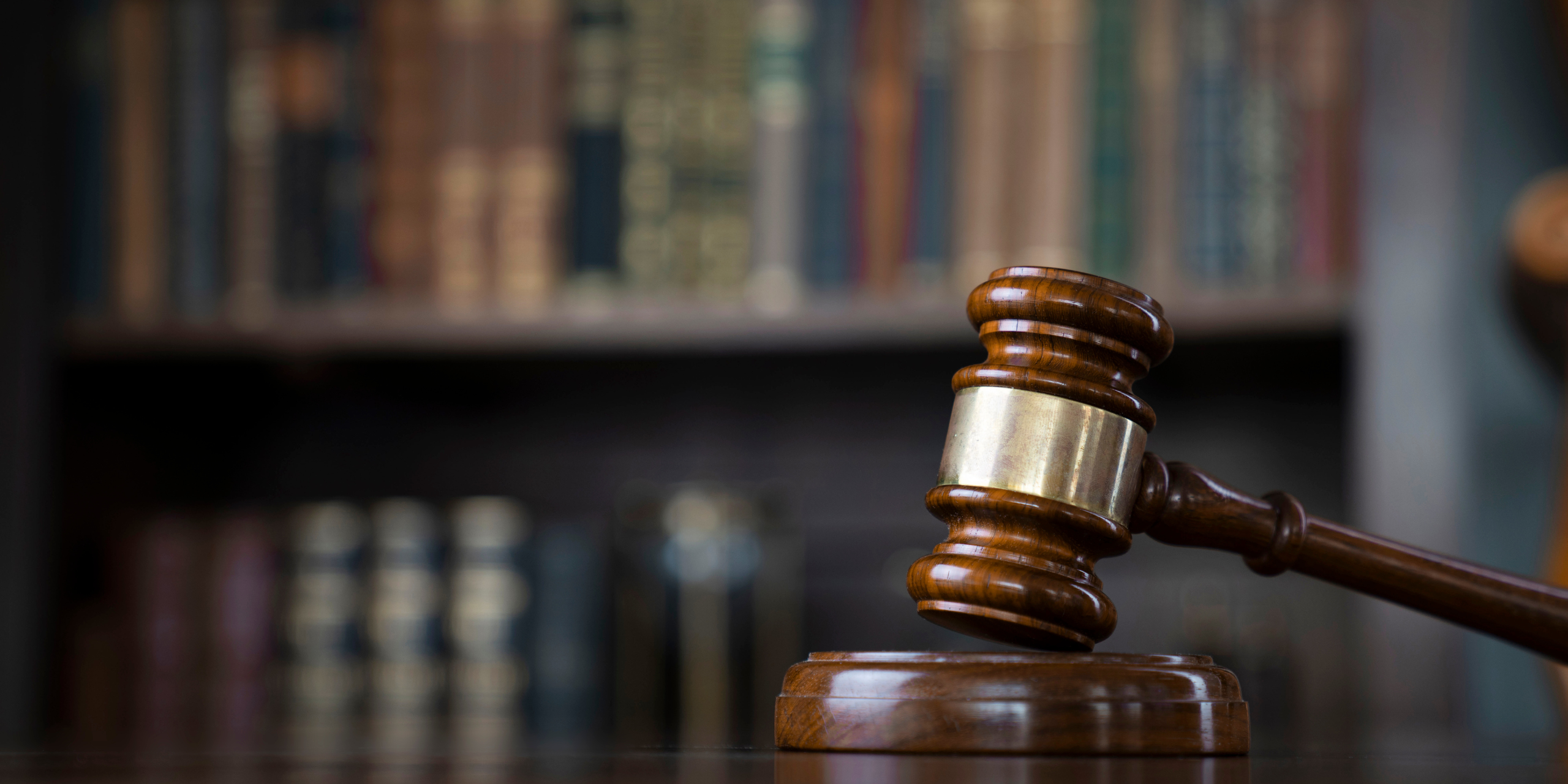 A gavel resting on a table in a room full of books.
