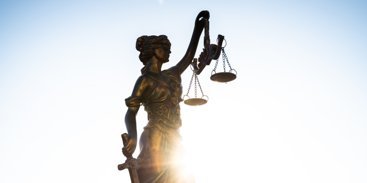 A statue of Lady Justice with the sun coming up behind it.